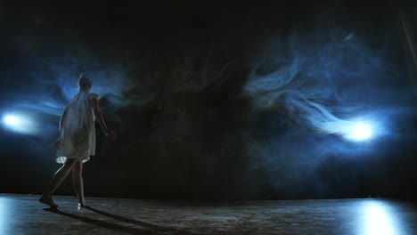 Moderner-Tanz:-Eine-Frau-Im-Weißen-Kleid-Tanzt-Ein-Modernes-Ballett-Und-Springt-Auf-Der-Bühne-Mit-Rauch-Im-Blauen-Scheinwerferlicht.